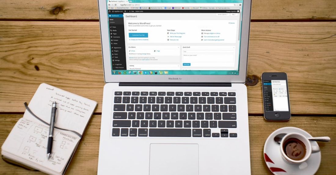 CMS - Turned-on Macbook Air Beside Black Iphone 4, Cup of Tea, and Notebook on Brown Wooden Surface